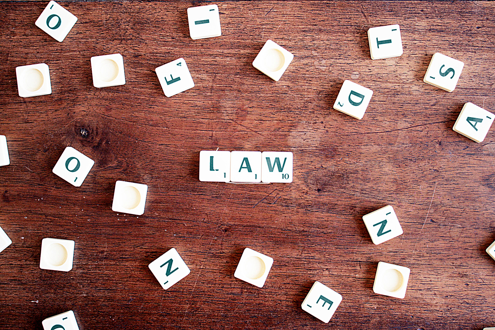 Scrabble tiles on a table with three tiles in the middle that spell out "law"