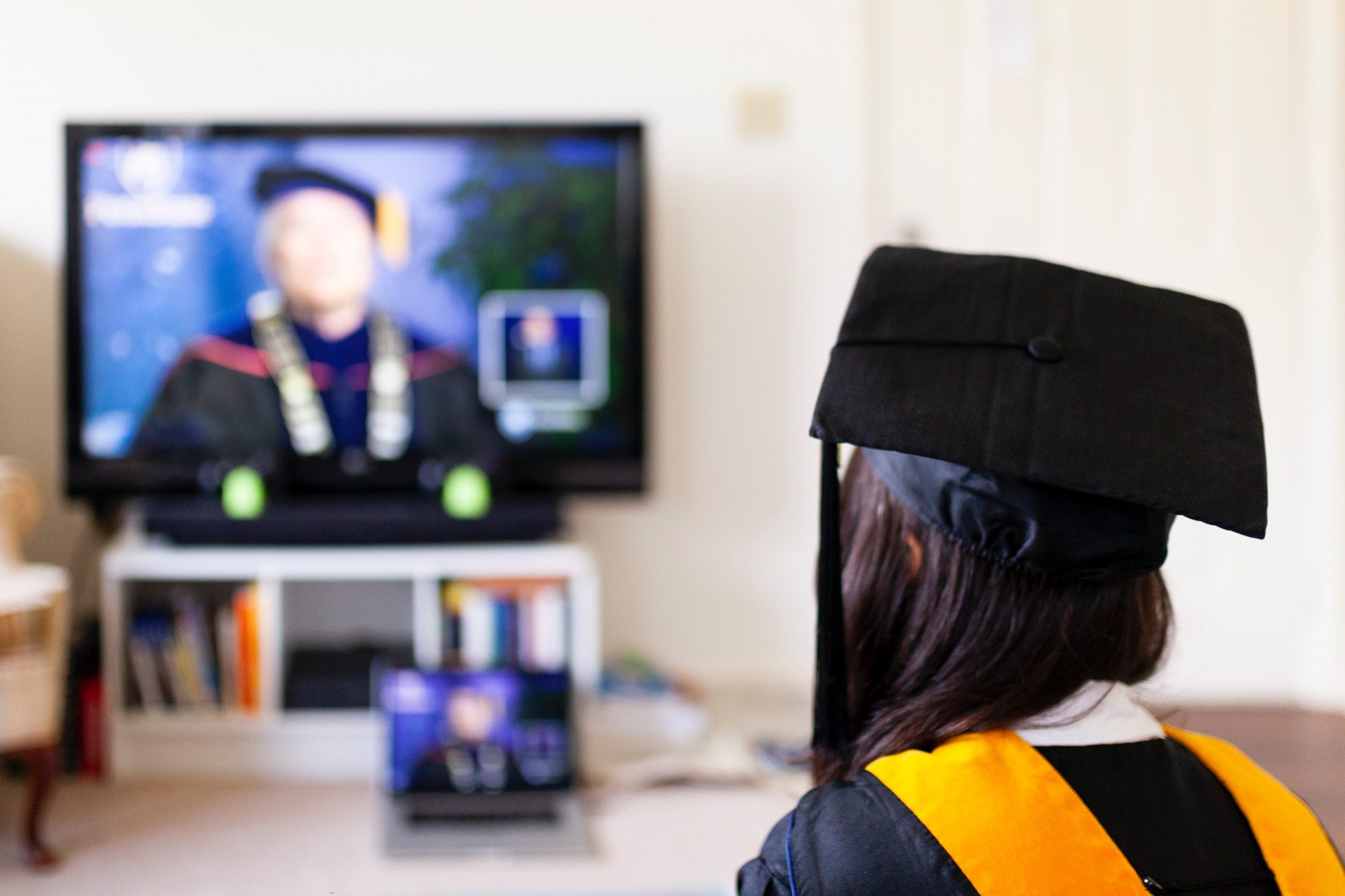 girl in cap and gown sits for virtual graduation