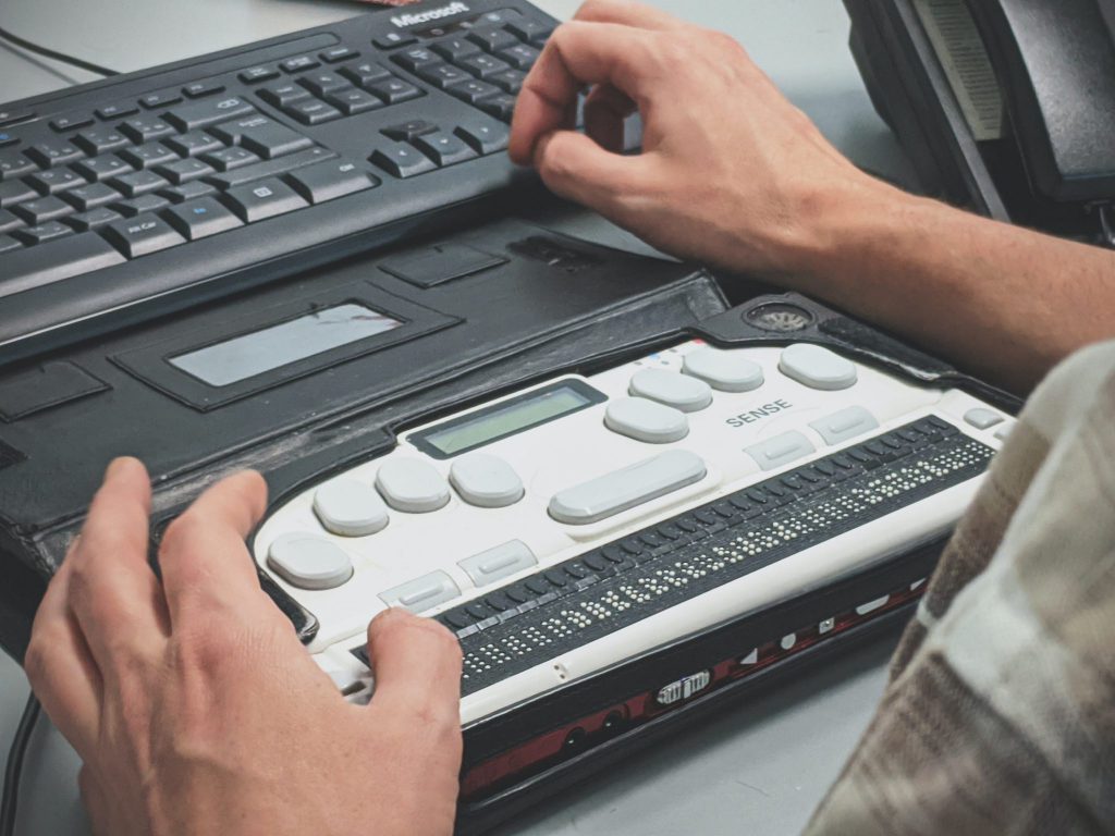 Man sits at desk using a refreshable braille display.