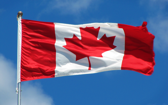 Canadian Flag with Red Maple Leaf on a white background with red bars on the left and right side flying in a blue sky