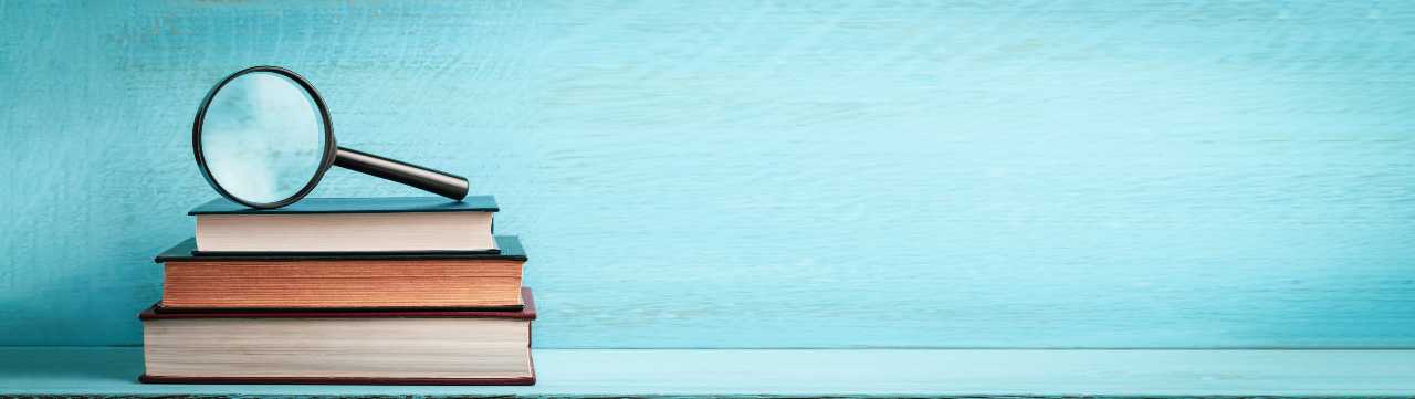 3 stacked books with a magnifying glass on top